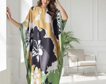 Op de afbeelding: Een lange kaftan jurk met een bloemenprint in zwart, wit, geel en groen. De jurk heeft een losse, comfortabele pasvorm en is afgewerkt met een groene rand. Het woord "Kaftan" staat op de jurk.