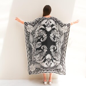 May include: A black and white patterned kaftan with a floral and leaf design. The kaftan is made of a lightweight fabric and has a flowing silhouette.