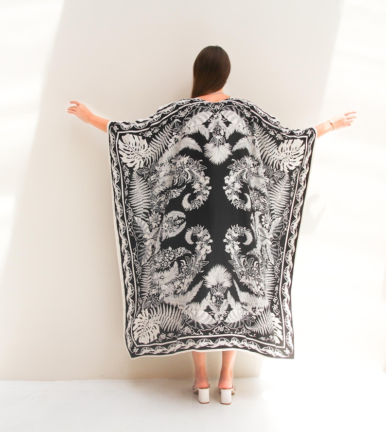 May include: A black and white patterned kaftan with a floral and leaf design. The kaftan is made of a lightweight fabric and has a flowing silhouette.
