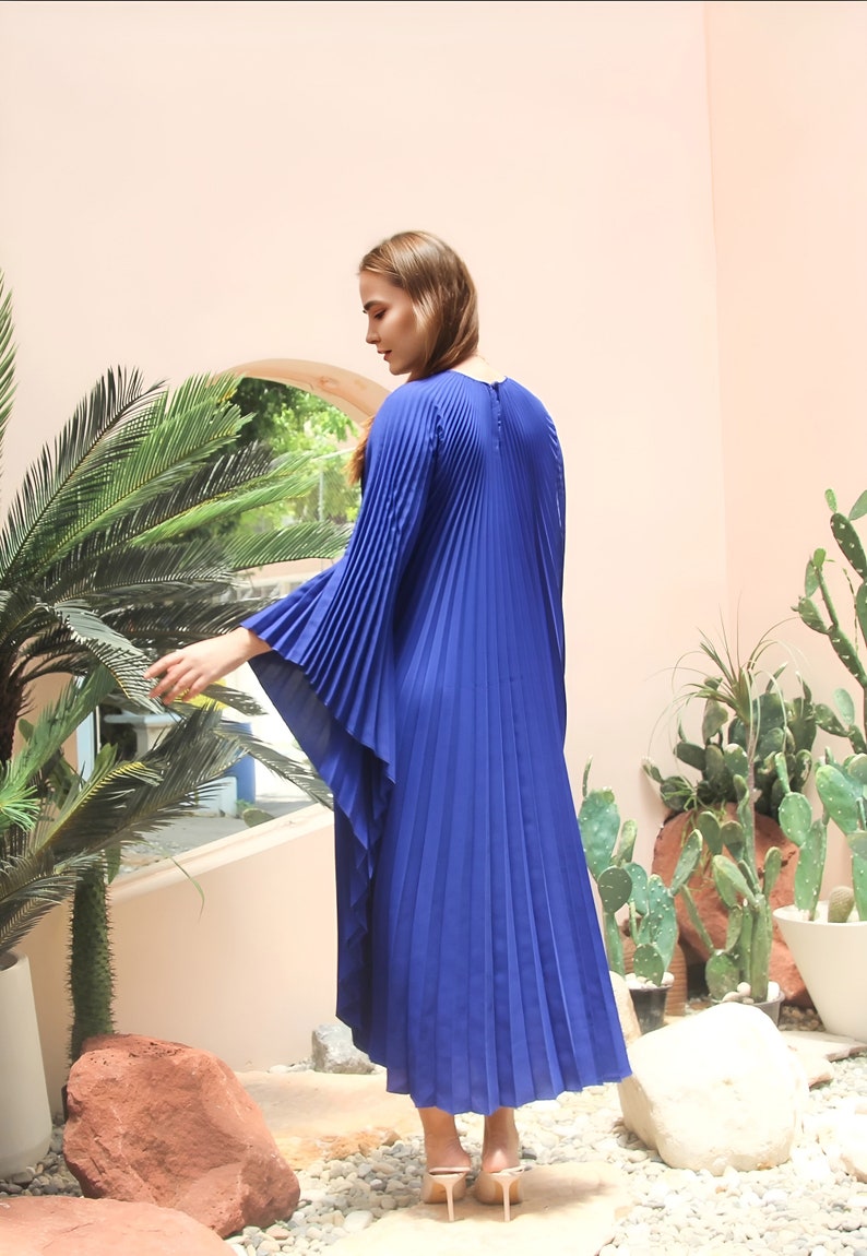 May include: A royal blue maxi dress with pleated detailing and long, flowing sleeves. The dress is made of a lightweight fabric and has a relaxed fit.