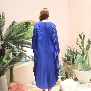 May include: A royal blue pleated maxi dress with long sleeves and a high neckline. The dress has a flowing, A-line silhouette and is made of a lightweight, soft fabric.