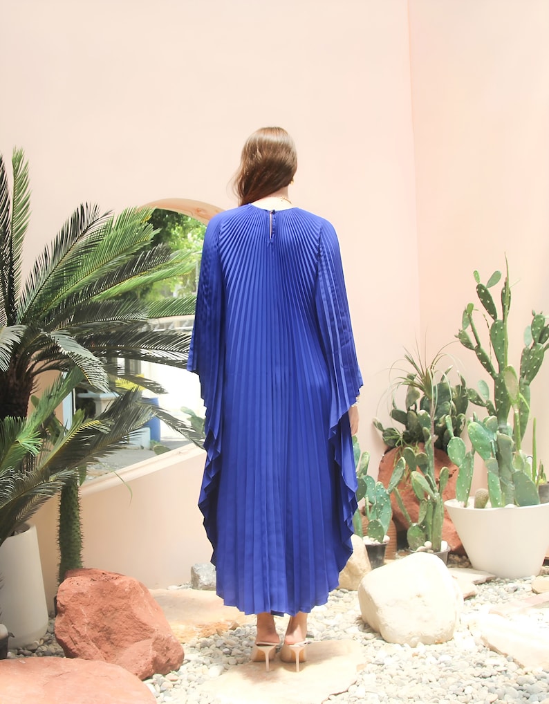May include: A royal blue pleated maxi dress with long sleeves and a high neckline. The dress has a flowing, A-line silhouette and is made of a lightweight, soft fabric.
