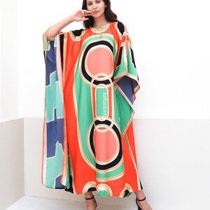 May include: A long, flowing kaftan with a geometric print in shades of orange, green, blue, and black. The kaftan has a wide, flowing silhouette and a round neckline.