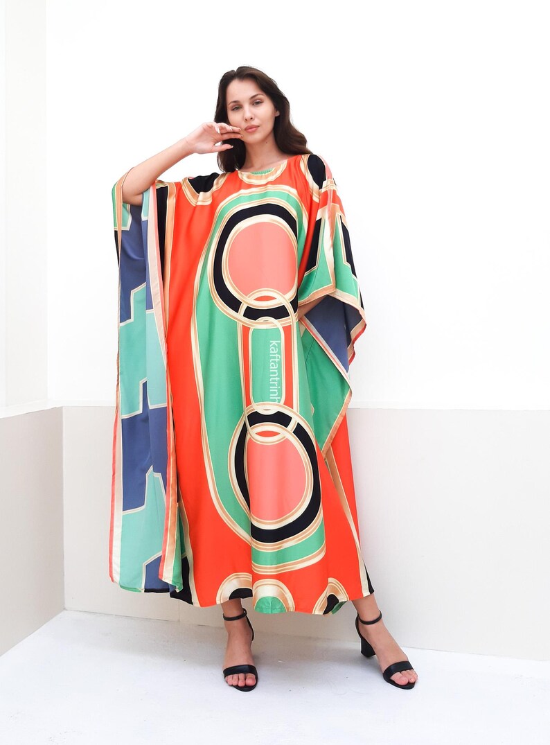 May include: A long, flowing kaftan with a geometric print in shades of orange, green, blue, and black. The kaftan has a wide, flowing silhouette and a round neckline.