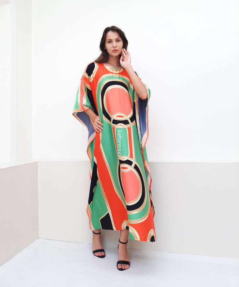 May include: A long, flowing kaftan with a geometric pattern in shades of green, orange, black, and white. The kaftan has a loose, comfortable fit and is perfect for warm weather.