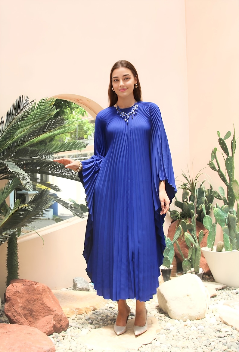 May include: A royal blue pleated maxi dress with long sleeves and a round neckline. The dress has a flowing, relaxed fit and features a decorative beaded necklace.