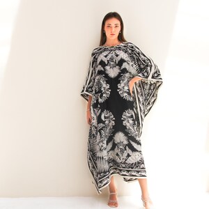 May include: A black and white maxi dress with a floral print. The dress has a loose, flowing fit and a wide neckline. The model is wearing the dress with white sandals.