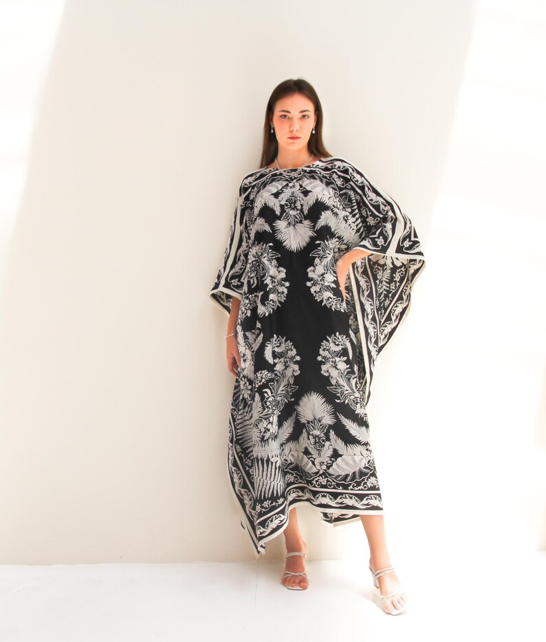 May include: A black and white maxi dress with a floral print. The dress has a loose, flowing fit and a wide neckline. The model is wearing the dress with white sandals.