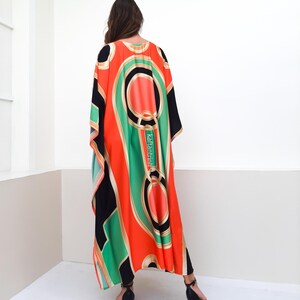 May include: A long, flowing kaftan with a geometric print in shades of black, green, orange, and gold. The kaftan has a loose, comfortable fit and is perfect for warm weather.
