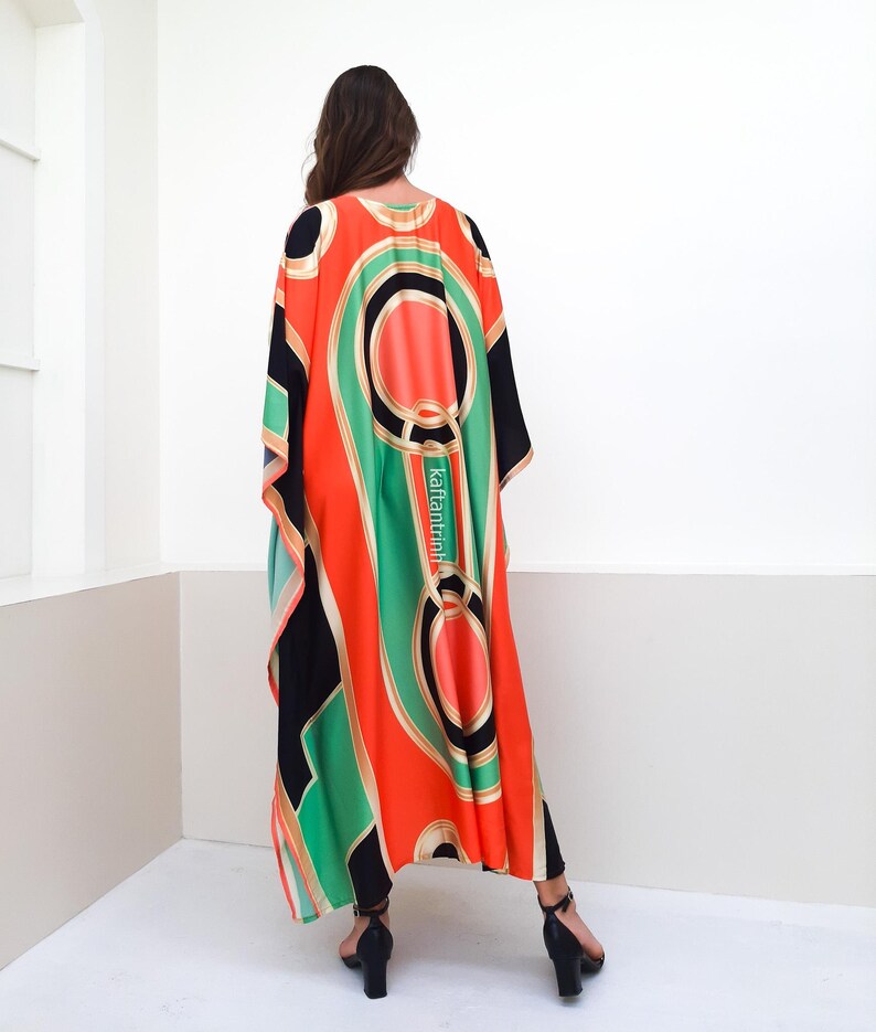 May include: A long, flowing kaftan with a geometric print in shades of black, green, orange, and gold. The kaftan has a loose, comfortable fit and is perfect for warm weather.