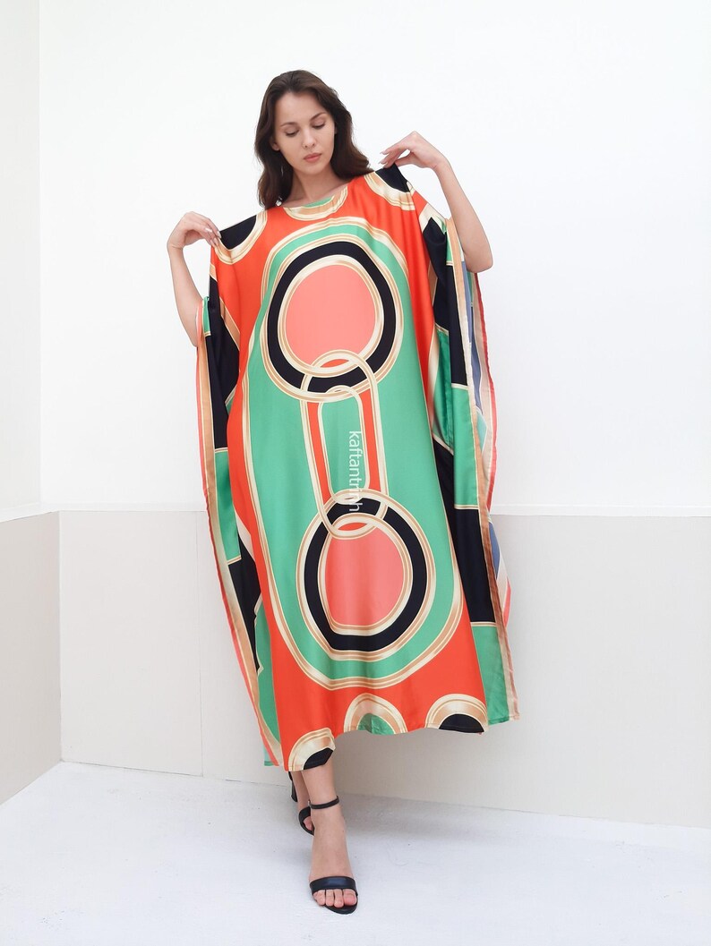 May include: A long, flowing kaftan with a geometric print in shades of orange, green, black, and white. The kaftan has a round neckline and a relaxed fit.