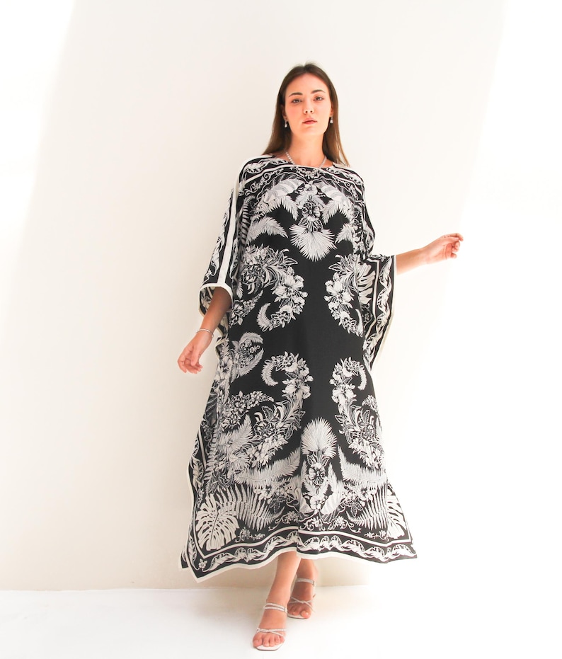 May include: A black and white patterned kaftan with a floral design. The kaftan has a long, flowing silhouette and a wide, open neckline.