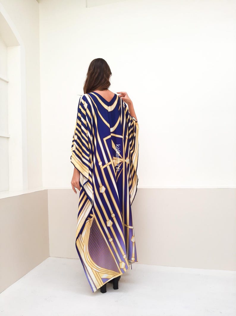 May include: A long, flowing kaftan with a geometric pattern in shades of blue, gold, and white. The kaftan has a V-neck and long sleeves.