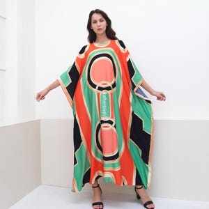May include: A long, flowing, orange, green, and black kaftan with a geometric pattern. The kaftan has a round neckline and wide sleeves.