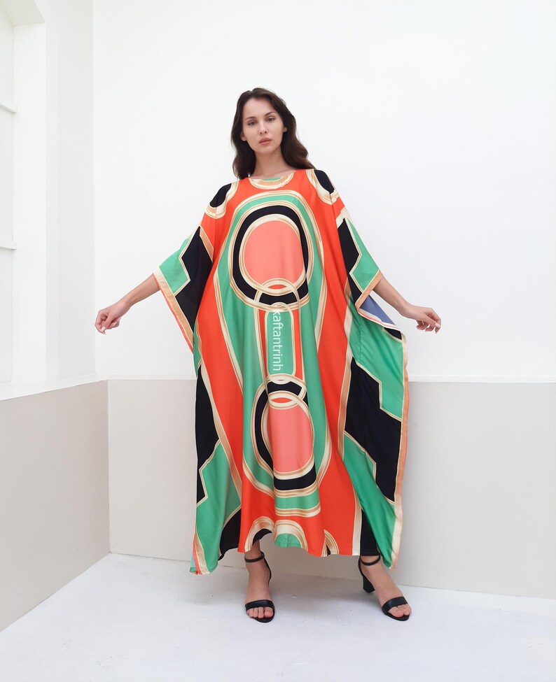 May include: A long, flowing, orange, green, and black kaftan with a geometric pattern. The kaftan has a round neckline and wide sleeves.