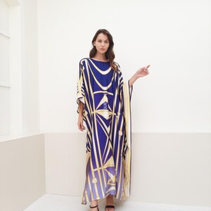 May include: A long, flowing blue and gold patterned kaftan with a geometric design. The kaftan has a wide, flowing neckline and long sleeves. The model is wearing black heeled sandals.