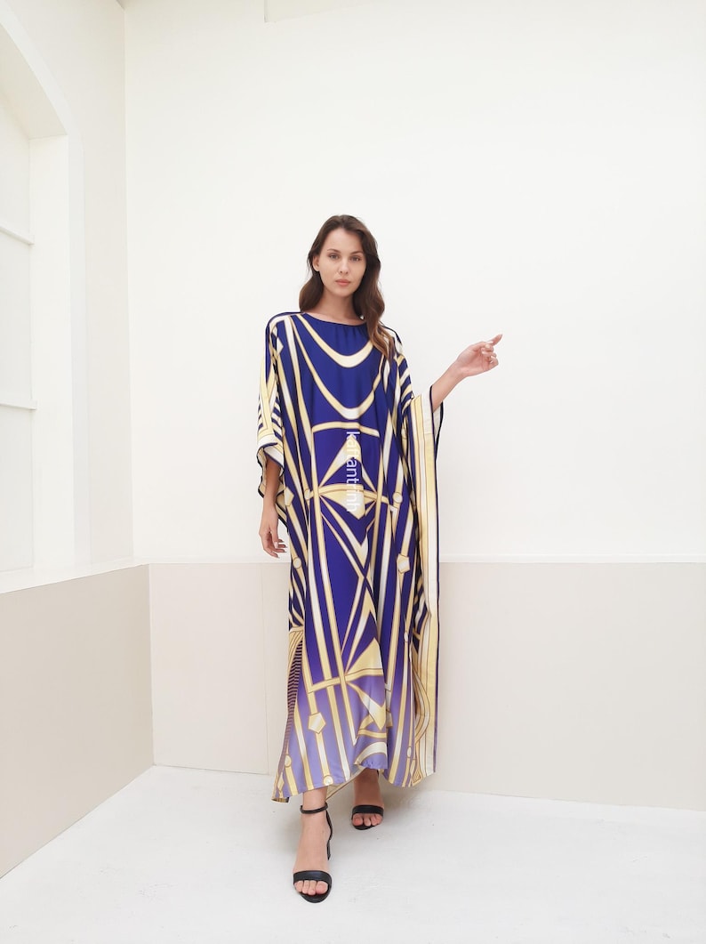 May include: A long, flowing blue and gold patterned kaftan with a geometric design. The kaftan has a wide, flowing neckline and long sleeves. The model is wearing black heeled sandals.