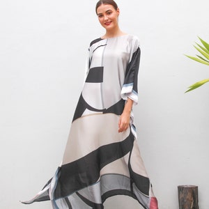 May include: A long, flowing dress with a geometric pattern in black, white, beige, and grey. The dress has a loose fit, wide sleeves, and a flared skirt. The model is wearing black high-heeled sandals.