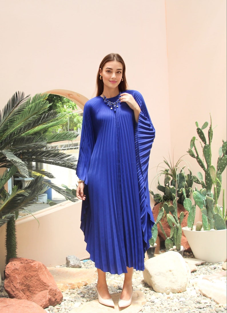 May include: A royal blue pleated maxi dress with long sleeves and a high neckline. The dress has a flowing, relaxed fit and is perfect for a summer evening.