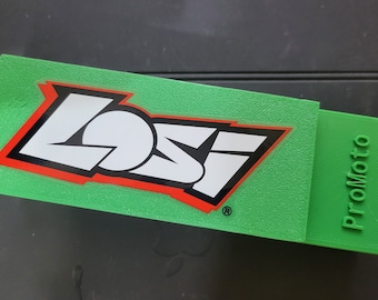 May include: Green plastic box with the word "Losi" in white letters with a red outline and black lettering. The box has the word "ProMoto" printed on the side.