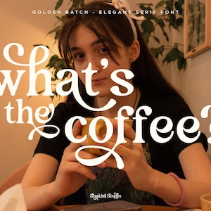 Op de afbeelding: Een persoon die een gele mok vasthoudt met de tekst "what's the coffee?" in een wit elegant schreeflettertype. De tekst "GOLDEN BATCH - ELEGANT SERIF FONT" staat bovenaan. Het Shakini Studio-logo staat onderaan.