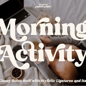 May include: A white retro font design with the text "Morning Activity" in a stylized font with ligatures. The text is on a background of a person sitting on a bed with a laptop and a cup of coffee.