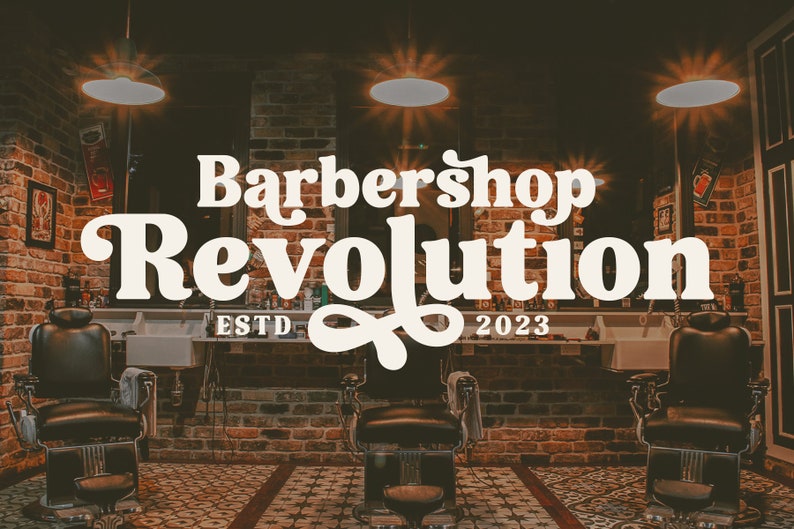 Op de afbeelding: Een barbershop interieur met bakstenen muren, vintage verlichting en twee zwarte leren kappersstoelen. Het bord boven de stoelen luidt "Barbershop Revolution ESTD 2023".