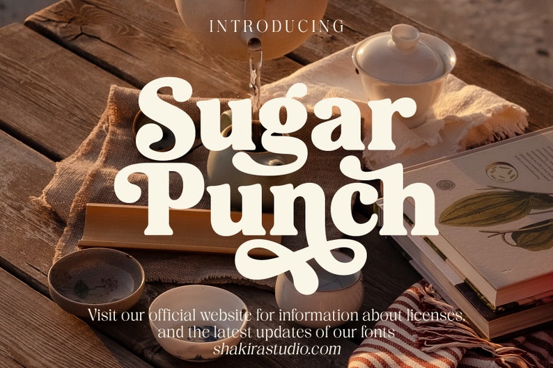 Op de afbeelding: Introductie van het lettertype Sugar Punch, een retro-ge&iuml;nspireerd lettertype met een speelse, grillige uitstraling. Het lettertype wordt weergegeven op een rustieke houten tafel met een theepot, theekopjes en boeken. Bezoek shakirastudio.com voor meer informatie.