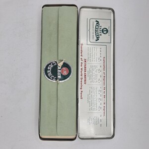 Op de afbeelding: Een open, vintage etui met een lichtgroene buitenkant en een zilveren binnenkant. De etui heeft het "AW Faber-Castell" logo en de tekst "Standard of the World Drawing Pencil".