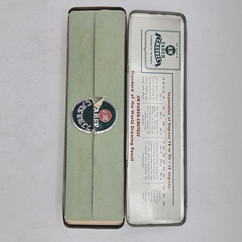Op de afbeelding: Een open, vintage etui met een lichtgroene buitenkant en een zilveren binnenkant. De etui heeft het "AW Faber-Castell" logo en de tekst "Standard of the World Drawing Pencil".