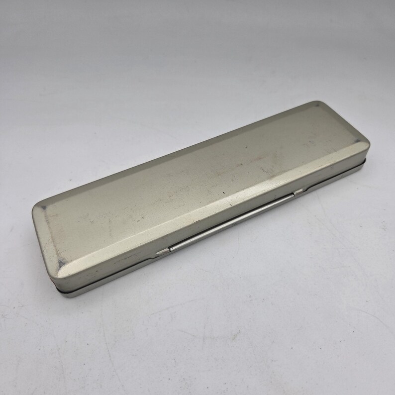 Op de afbeelding: Een rechthoekige, zilverkleurige metalen etui met een scharnierend deksel. De etui heeft een geborstelde afwerking en een eenvoudig, functioneel ontwerp. De etui is gesloten en lijkt leeg te zijn.