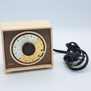 May include: A beige and brown vintage Sears clock radio with a round dial and a black cord.