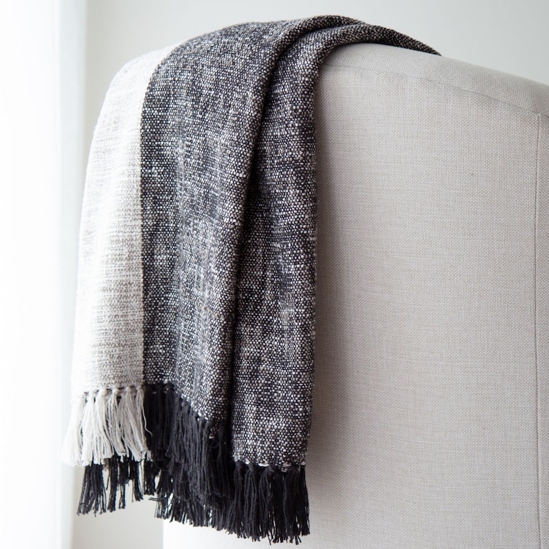 May include: A black and white striped throw blanket with fringe on the edges. The blanket is draped over a chair.