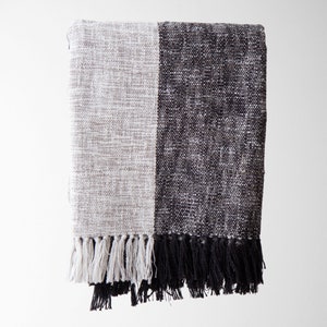 May include: A black and white woven throw blanket with fringe. The blanket is made of a soft, textured fabric and has a modern, minimalist design.