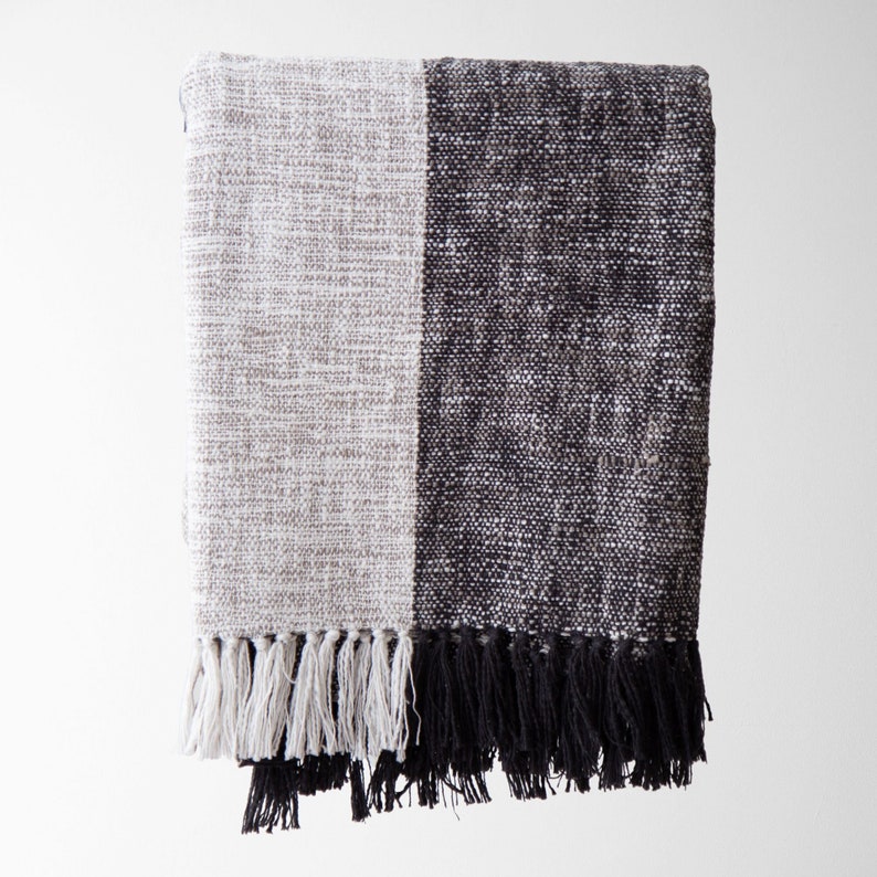 May include: A black and white woven throw blanket with fringe. The blanket is made of a soft, textured fabric and has a modern, minimalist design.
