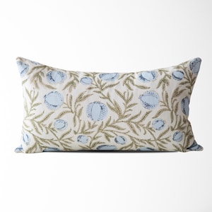 May include: Rectangular decorative pillow with a floral pattern. The pillow features a cream-colored background with a repeating design of light blue fruit and olive-green leaves and vines. The pillow is approximately 20 inches long.