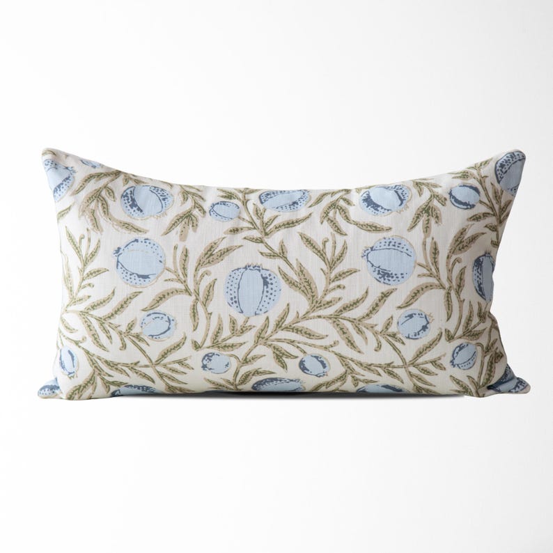 May include: Rectangular decorative pillow with a floral pattern. The pillow features a cream-colored background with a repeating design of light blue fruit and olive-green leaves and vines. The pillow is approximately 20 inches long.