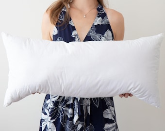 May include: A white rectangular pillow held in front of a person wearing a blue and white floral dress.