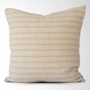 May include: A soft, cream-colored throw pillow with pink horizontal stripes. The pillow has a textured woven fabric with a subtle raised dot pattern.