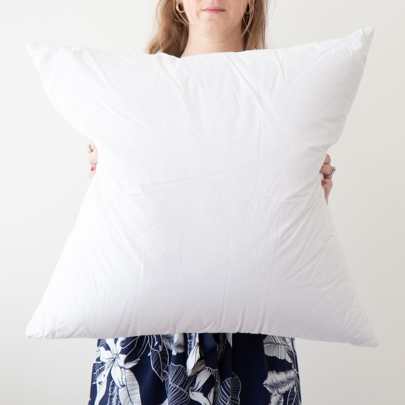 May include: A white pillow being held by a person. The pillow is large and fluffy.