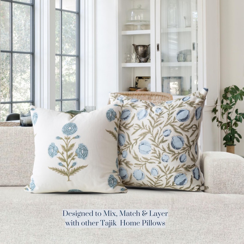 May include: Two decorative throw pillows with floral patterns. One pillow features a blue floral design on a white background, and the other has a blue and green floral pattern. The pillows are on a neutral-colored sofa. Text: Designed to Mix, Match & Layer with other Tajik Home Pillows.
