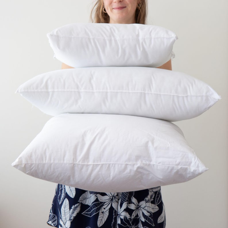 May include: A stack of three white pillows, held by a person wearing a floral dress.