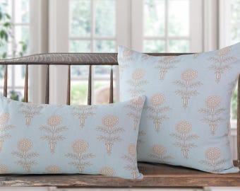May include: Two decorative throw pillows with a light blue background and a repeating floral pattern in beige. One pillow is rectangular, the other is square. The pillows are resting on a wooden bench.