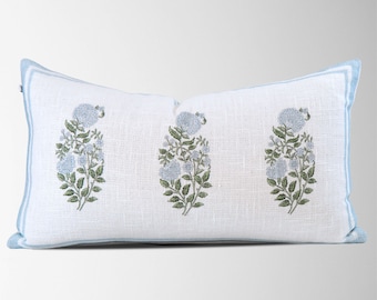 May include: A white rectangular pillow with a blue border and a floral pattern. The pillow features three clusters of light blue flowers with green leaves.
