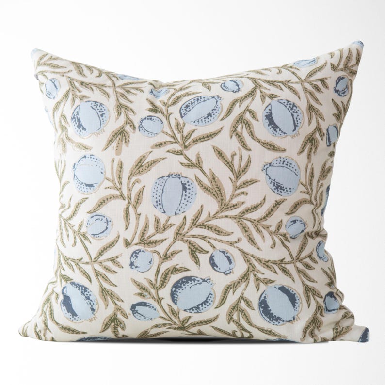 May include: Square decorative pillow with a repeating pattern of light blue fruit and olive-green leaves on a cream background. The pillow is a square shape and appears to be made of fabric. The design is a botanical theme.