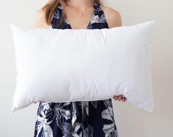 May include: A white pillow being held by a person wearing a blue and white floral dress.