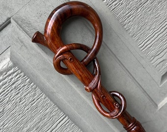 May include: A handcrafted wooden walking cane with a dark brown finish. The handle features a unique knot design and a curved top. The shaft is intricately carved, showcasing the natural wood grain. A stylish and functional accessory.