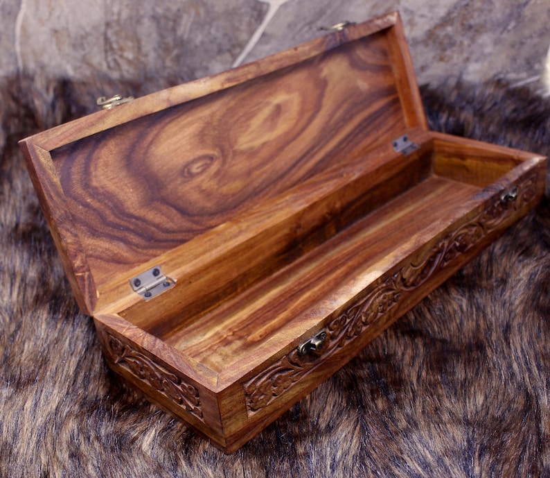 May include: Open wooden box with a hinged lid. The box is made of a rich, dark brown wood with visible grain patterns. The edges of the box are carved with floral designs. The box is open, revealing an empty interior.