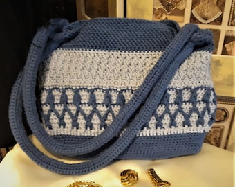 Op de afbeelding: Een blauwe en witte gehaakte tote bag met een geometrisch patroon. De tas heeft een enkele lange band.