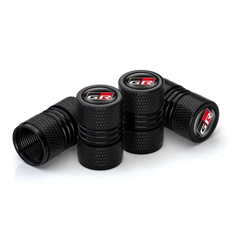 Puede incluir: Juego de cuatro tapones de v&aacute;lvula de metal negro con un logotipo "GR" rojo y blanco.